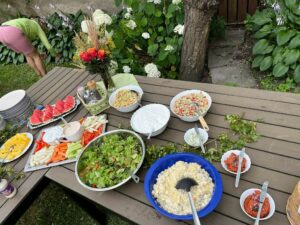 Holztisch mit vielen Schüsseln von Salat, Gemüse, Früchten aus dem Garten