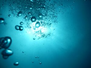 Blick von unten im Meer hoch zur hellen Wasseroberfläche mit sprudelnden Luftblasen