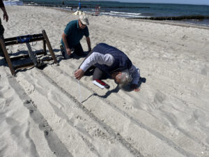 Ein Mann mit einem Maßband überprüft die Tiefe einer gezogenen Furche am Strand