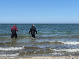 Zwei Männer gehen am Strand in wasserdichter Kleidung in die Ostsee