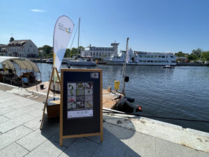 Aufsteller mit Einladungstext, Stiftungsfahne und Forschungsfloß am Hafen