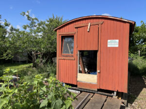 Bauwagen mit rot-orangenem Anstrich mit Bäumen und Pflanzen um ihn herum