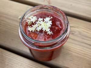 Offene Glas mit Erdbeermarmelade und Holunderblüte auf der Erdbeermasse