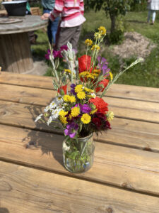 Ein Strauß handgepflückter Blumen in einem kleinen Glas auf einem Holztisch