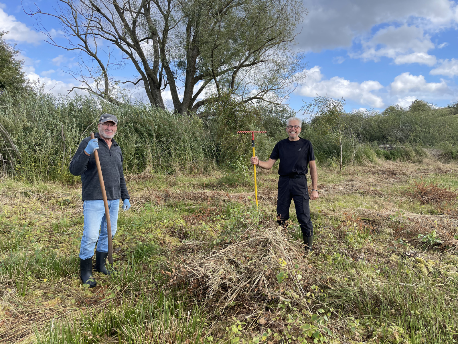Zwei Personen lachen und stehen im gemähten Moor mit Rechen in den Händen