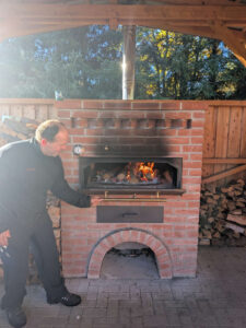 Ein Mann öffnet die Klappe eines gemauerten Holzbackofens.