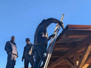 Ein Mann steht auf einer Leiter, die am Dach angelehnt ist