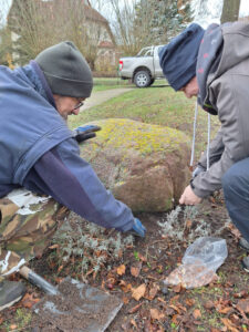 Zwei Personen an einem Stein mit Pflanzgerät