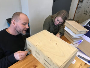 Zwei Personen an einer Holzkiste mit einem speziellen Mechanismus zum Öffnen