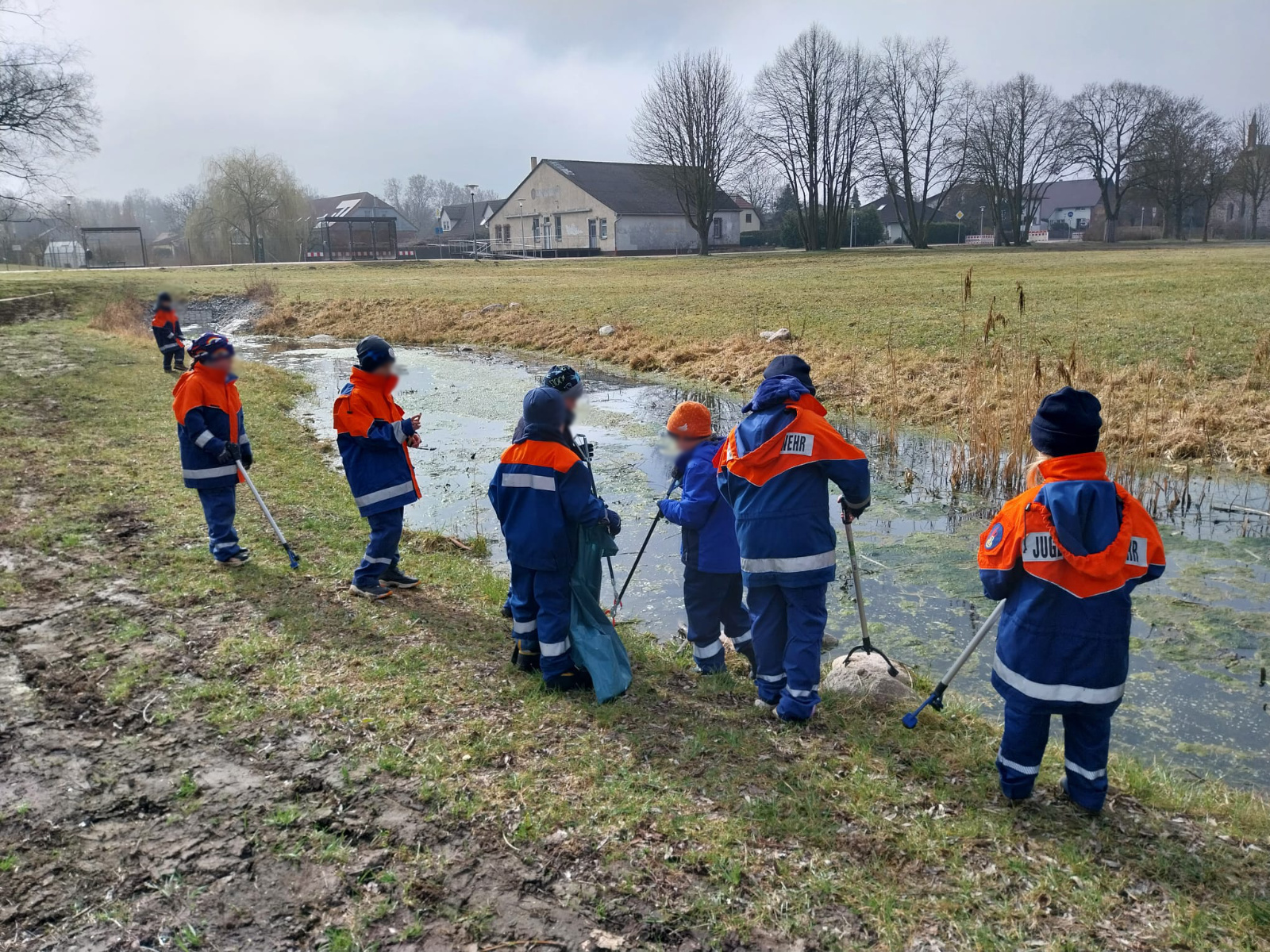 Kinder einer Jugendfeuerwehr sammeln Müll an einem Gewässer