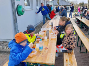 Kinder und Erwachsene sitzen auf Bierbänken an Tischen und essen etwas