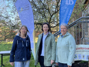Drei Personen stehen im Garten vor Fahnen von Klimastiftung MV und Internationalem Bund