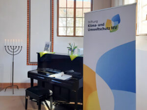 Roll-Up der Klimastiftung MV neben einem Klavier und einer Menora