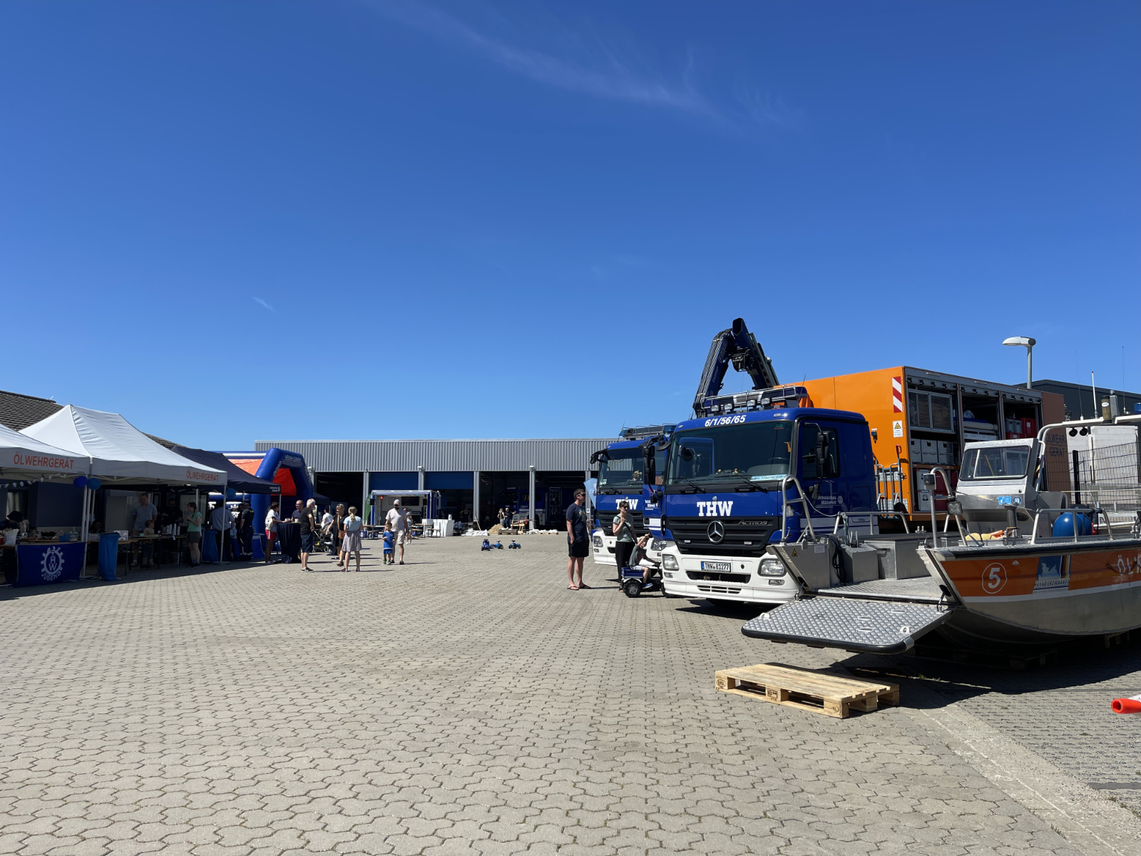 Gepflasterter Hof mit Großfahrzeugen, Essensständen und Hüpfburg des THW vor blauem Himmel