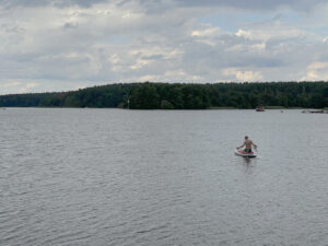 See mit Ufer im Hintergrund und Jugendlichem sitzend auf einem SUP